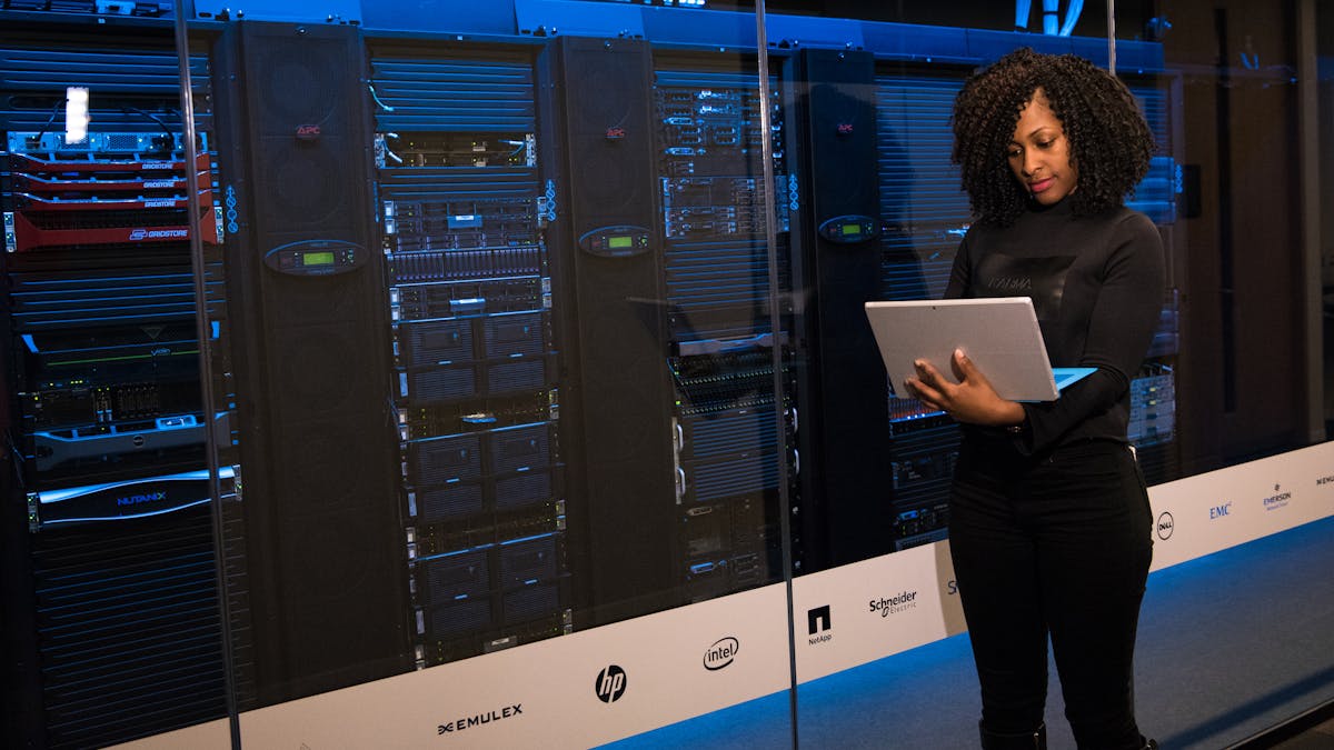 Engineer monitoring data servers in a server room with a laptop, representing alert and incident operations