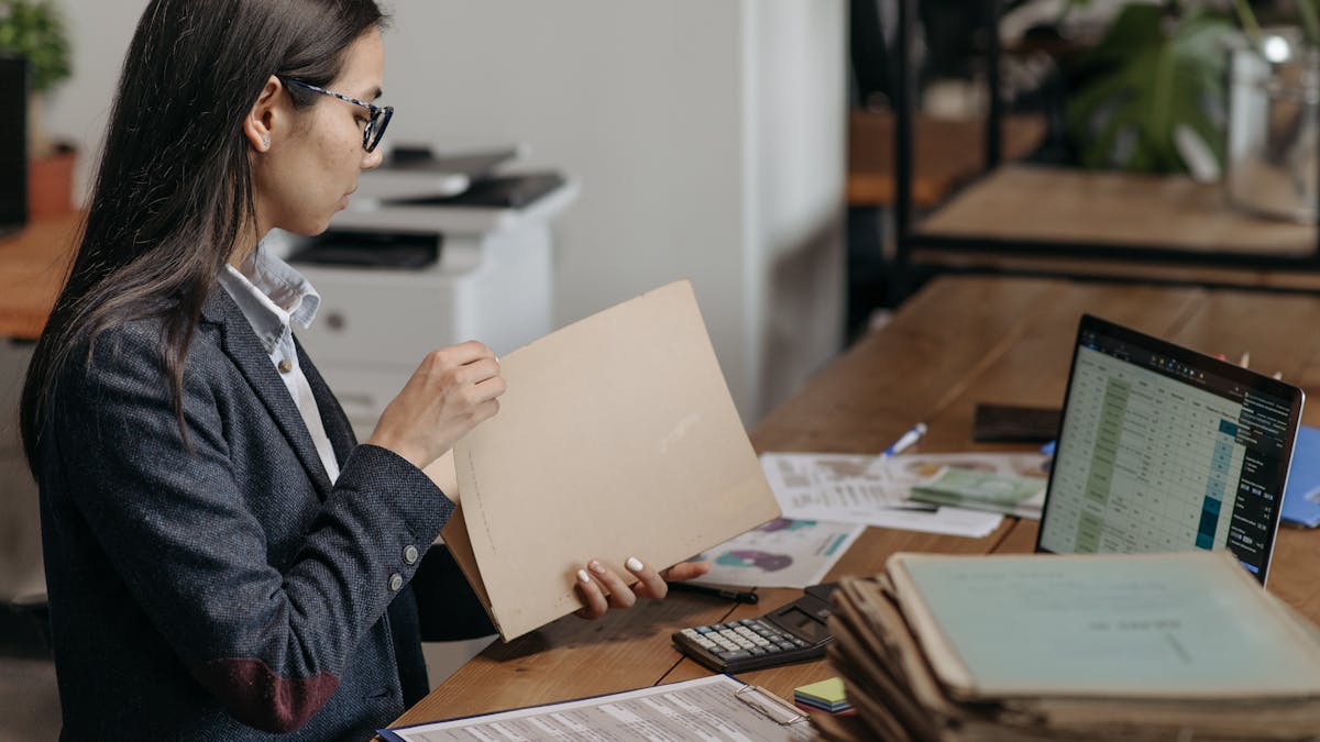 Professional reviewing documents at a desk with laptop and files, representing template and document management